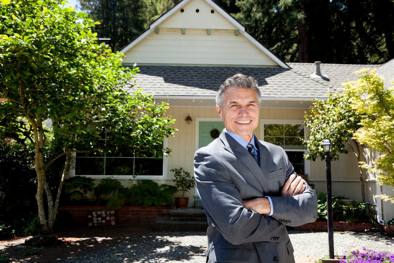 Man in suit smiles in front of house