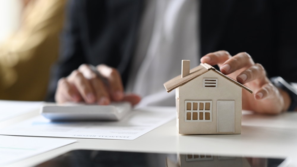 man using calculator with model of house